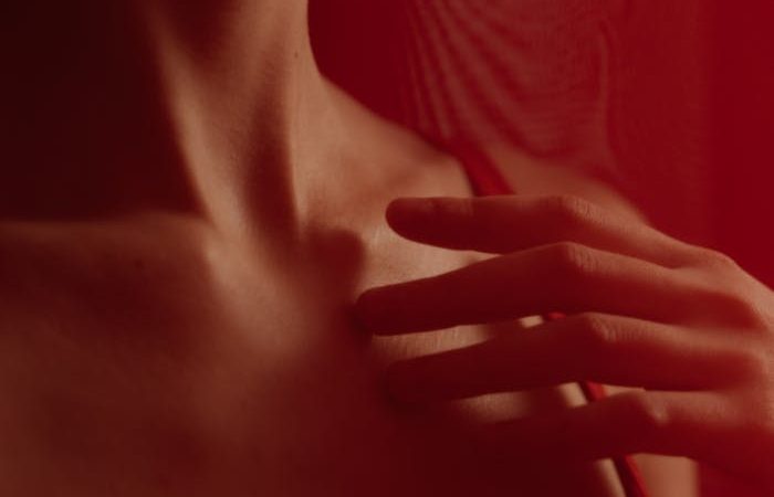 Close-up of a person touching their chest with hands in soft red lighting, evoking intimacy.