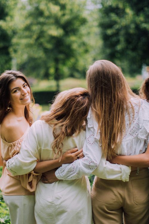 Four women enjoying a sunny day together in a green park, embracing each other and smiling.